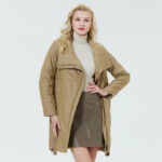 Parka matelassée femme avec col à revers marron, porté par une femme blonde debout, sur fond bleu clair.