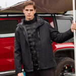 Parka courte homme avec capuche noire, portée par un homme, devant une voiture rouge