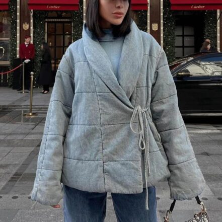 Mannequin femme brune portant une parka courte cache-cœur en jean. Elle est dans une rue.