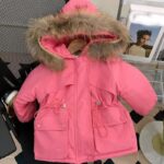Parka enfant rose, avec une capuche à fausse fourrure et deux poches plaqué, ainsi qu'un cordon pour ajuster la taille.