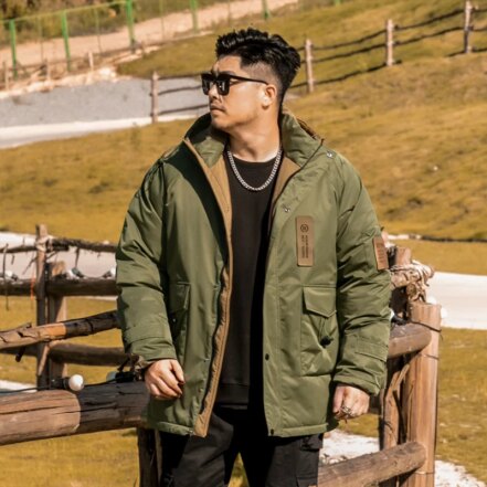 Parka militaire homme avec capuche et conception épaisse, de couleur kaki, porté par un homme avec lunette de soleil en extérieur dans un champs