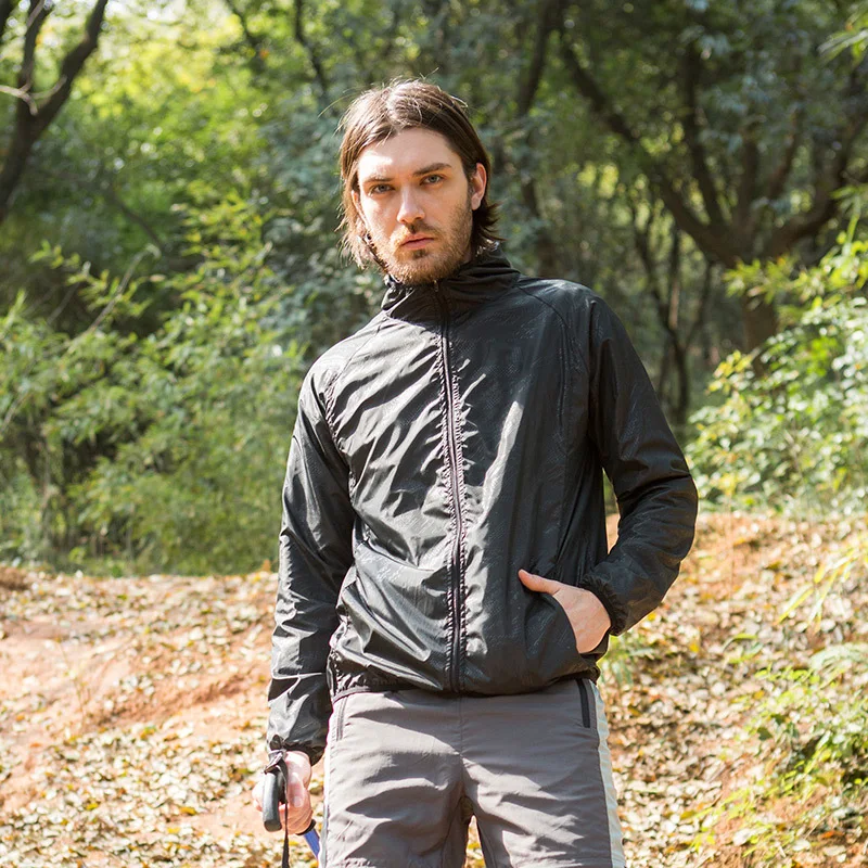 Parka pluie homme imperméable facilement transportable Parka pluie homme imperméable facilement transportable, de cculeur noire, porté par un homme debout dans la forêt