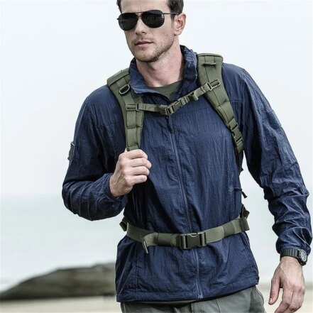 Parka pluie homme légère et imperméable à séchage rapide, de couleur bleue, porté par un homme avec lunettes de soleil et un sac militaire sur le dos, de face.